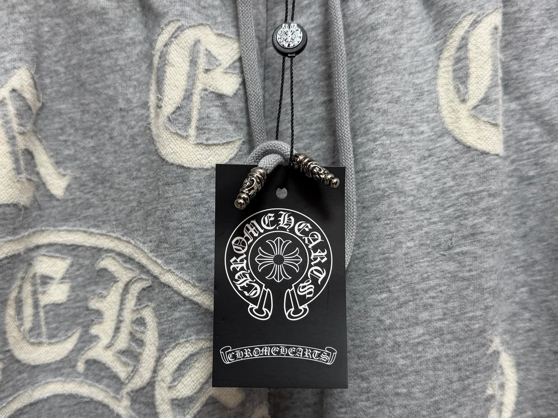 CH/Cro Heart 2026ss Burnt Flower Straight-leg Sweatpants Classic heavy-weight sweatpants with gray tones, Retro street style full-fitting, direct recognition, same style for men and women. ●Three-dimensional patchwork technology: The whole body is covered with Gothic letters + cross flower totems, using raw edge patchwork embroidery, with a mustache-like old texture, and uneven and layered patterns. It is not an ordinary print, and it is durable and not easy to fall off. ●Style tailoring: Loose, straight and wide-legged version, modifying the shape of the legs, hiding the flesh neatly, not flattering the figure, with an online drape, and the upper body has a relaxed street tone. ●Fabric and waist: Heavy knitted terry fabric, thick and soft, with good drape; elastic drawstring waist, with branded metal engraved rope ends, easy to put on and take off, and strong waist adaptability. ●Detailed design: The side pockets are convenient for carrying items, and the back pocket is decorated with cross-pattern patches. The front and rear patterns echo each other. Every detail is highly recognizable to the brand. ●Wearing scenarios: Suitable for street wear, daily outings, and trendy wear. Paired with sweaters, denim jackets, and leather jackets, you can easily create an American retro cool style. ●The overall gray base is paired with Cream White patches, which are low-key yet impactful. They are both comfortable and trendy. Versatile sweatpants, a must-have for fashionistas, are also available at the counter. SIZE：M L XL XXL XXXL